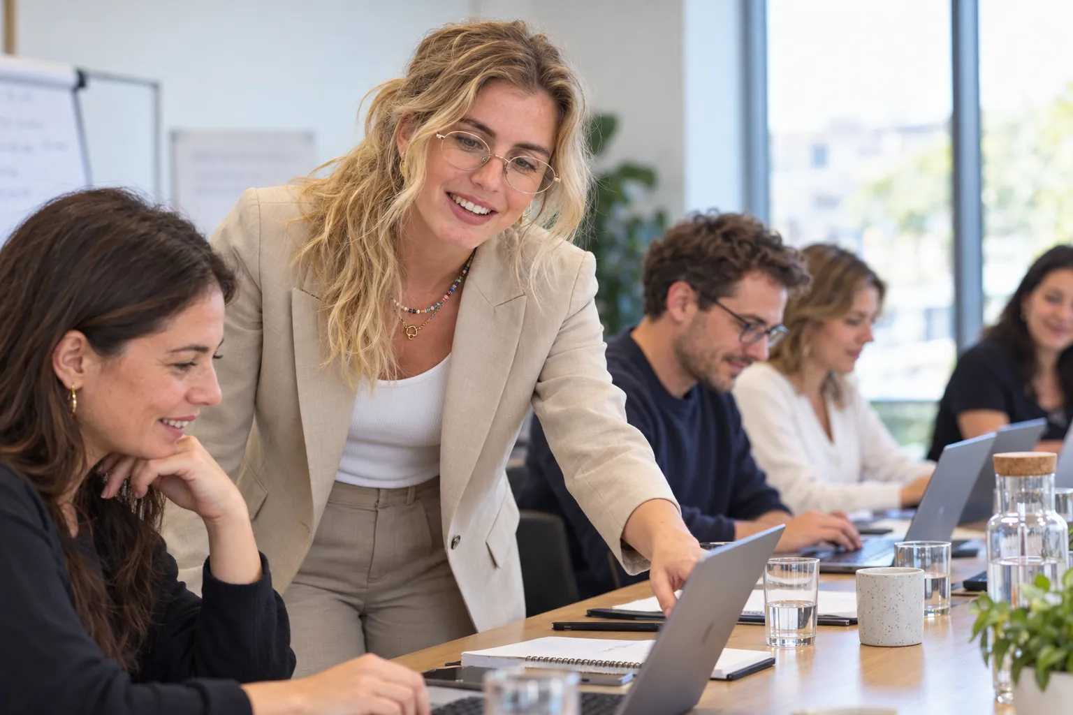 Candice Collange, penchée sur la table, accompagne une participante sur son ordinateur pendant une formation à l'IA générative